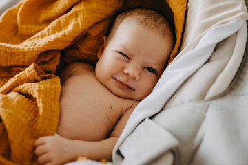 Closeup of a newborn baby making funny face, winking and smiling. - obrazy, fototapety, plakaty