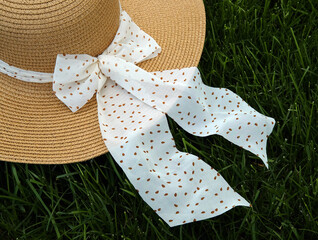 A straw hat with a cloth bow lies on the grass