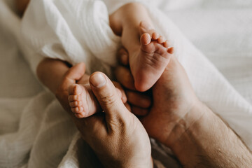Closeup of father holding small newborn baby feet in big hands.