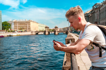 A young man uses a smartphone while walking along the embankment in the center of St. Petersburg in the summer