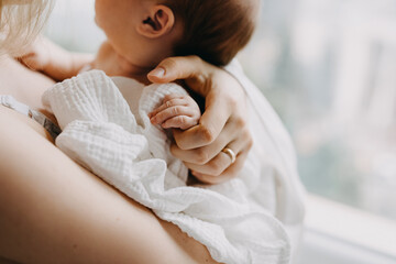 Obraz na płótnie Canvas Closeup of mother holding newborn baby hand, standing by the window.
