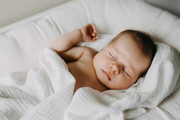 Newborn baby sleeping in a baby nest, covered with white blanket.