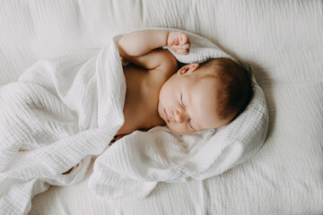 Newborn baby sleeping in a baby nest, covered with white muslin blanket.