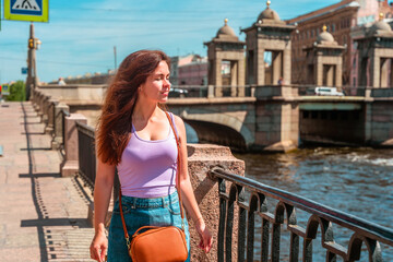 A beautiful young woman walks in the center of St. Petersburg on the embankment with a beautiful bridge