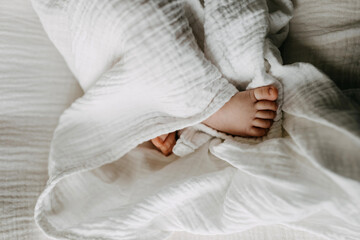 Closeup of newborn baby feet, covered with white blanket. - obrazy, fototapety, plakaty