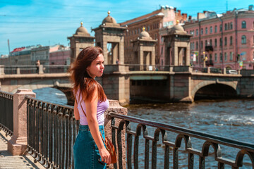 Fototapeta na wymiar A beautiful young woman walks in the center of St. Petersburg on the embankment with a beautiful bridge