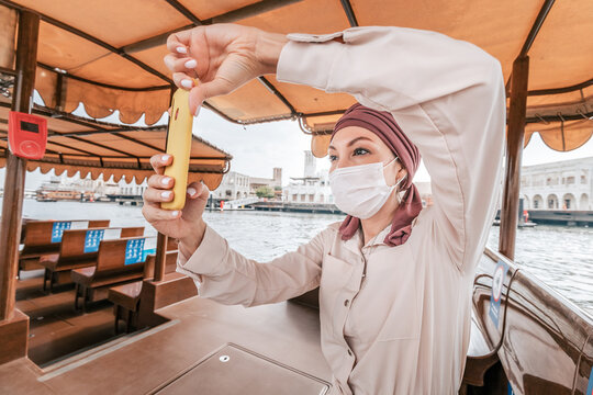 woman wearing medical face mask takes pictures on her smartphone while cruising on a traditional Abra Dhow boat on Dubai Creek. Travel in UAE concept