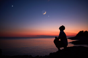 Silhouette of a man looking at the Moon and stars over sea ocean horizon. - Powered by Adobe
