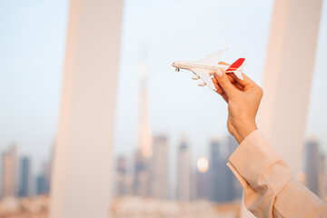 Woman holds a toy airplane in her hand against the backdrop of downtown Dubai with skyscrapers and the Burj Khalifa tower. Air travel and vacation flights in the UAE