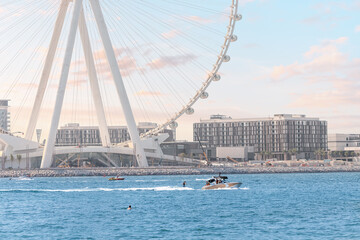 Tourists are entertained by water sports and attractions against the backdrop of the famous huge Ferris wheel Dubai Eye