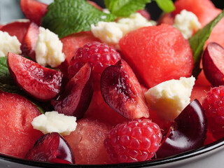 Fruit salad with feta cheese from watermelon, cherry and raspberry in a gray cup with a mint leaf.