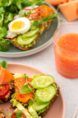 Healthy tasty breakfast, sandwiches with avocado and salmon, cucumbers and tomatoes, radishes and microgreens of peas with boiled egg and root salad, grapefruit smoothie in a glass