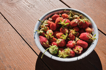 Young strawberries in a metal bowl on a wooden table