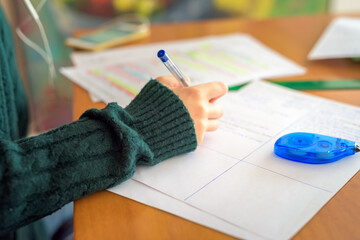 Joven con jersey verde escribe un papel con bolígrafo azul y escucha música en el móvil