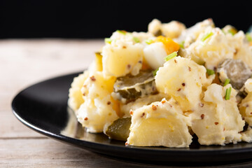 Potato salad with gherkins, egg and mustard on wooden table