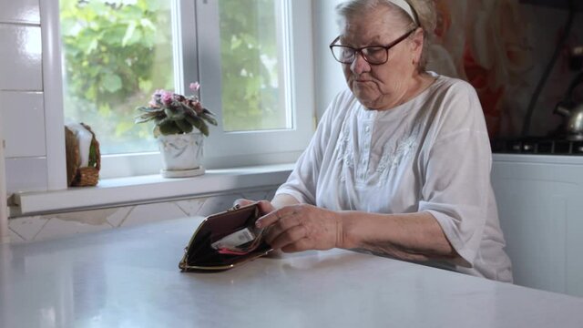 The older woman counts the money. An elderly woman Caucasian old woman gray-haired grandmother takes money out of her purse and counts it. Old hands hold bills. 
