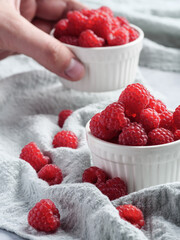 Fresh raspberries in small white cups on a table covered with cloth. A man's hand raises a cup.