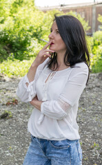 A young woman in a white blouse is smoking outside.