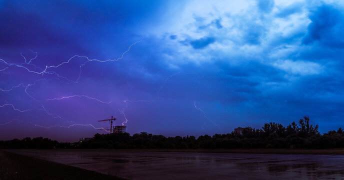 Landscape photo of big thunderclouds with many thunders raining down - nice purple and blue sky colors - old german runway in the foreground