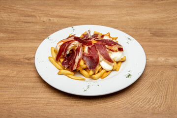 Round plate with lid to share with broken eggs with Serrano ham and French fries on light wood