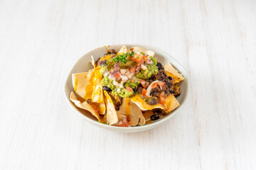 bowl of nacho juarez with guacamole, chopped onion, chili-stewed beans, wheat nachos and chopped chives