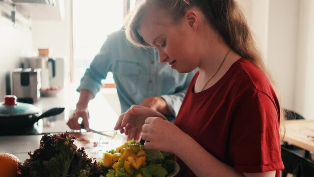 A young girl with down syndrome is cooking salad with her mother at home
