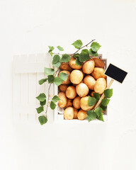 Young, natural, farm potatoes in a white wooden box and leaves on a white background. Selling seasonal vegetables at the local market. Support local farmers concept. Flat lay