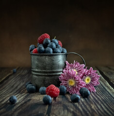 Blueberries and raspberries in a vintage cup on a dark background. Vintage metal mug. Chrysanthemums. Photo in Rustic style. Postcard. Copy space. High quality photo