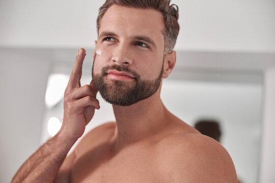 Handsome Middle Aged Man Applies Cream Onto Cheek In Bathroom