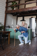 Senior woman helping sick husband with crutch at home