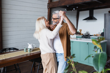 Side view of cheerful senior woman dancing with husband at home
