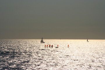 Calm sea with sunset sky and sun with windsurfer silhouettes over sea sunset, panoramic beach...