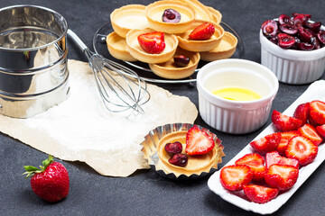 Sieve and flour on paper. Strawberries on plate. Sweet cherries in bowl.