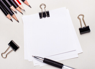 On a light background, black pencils, black paper clips, a pen and a blank sheet of white paper...