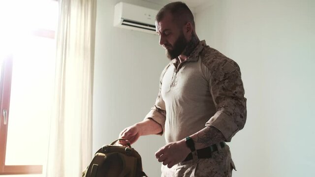 A serious military man wearing a uniform is taking his backpack and go away from home