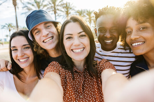 Group of happy multiracial people taking a selfie with mobile phone with back sunlight - Multiethnic friends in summer clothes having fun on holidays - Friendship and summer vacation concept