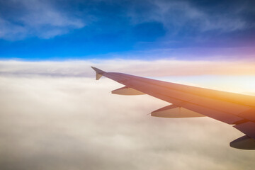 Fototapeta premium Flying and traveling, view from airplane window on the wing on sunset time. Aircraft wing under the earth and clouds. Flight in sky. Looking over aircraft wing in flight.