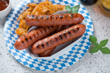 Blue and white carton plate with grilled german bratwurst sausages and sauerkraut, studio shot on a beige granite background