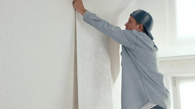 4K. Man applying a roll of wallpaper to the wall, smoothes fresh pasted wallpaper. Renovation of the apartment. interior design and Room renovations at house. Preparation for repair in the apartment