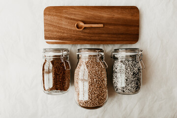 Glass jars full with dried uncooked food ingredients and wooden spoon on brown tray	