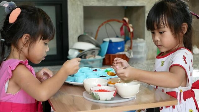 Cute siblings girls are scooping small pieces of Pipo jelly in different colors in a mold to prepare for dessert. Children make jelly desserts in the kitchen at home together.