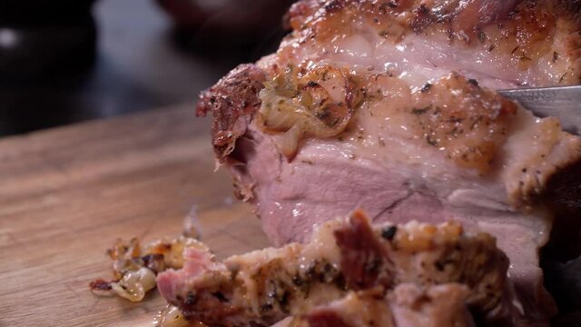 Close-up tracking shot of slicing a baked pork shoulder with a chef knife