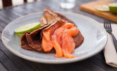 healthy breakfast of pieces of salted smoked salmon with buckwheat pancakes and lime