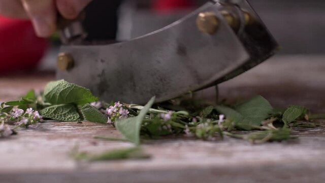 Mezzaluna mincing knife chopping fresh herbs on cutting board