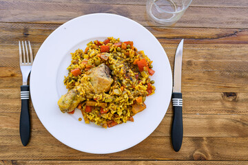 Typical Spanish food chicken rice or chicken paella. Overhead close-up of a portion of chicken leg with rice served in a white plate on a wooden table. Ethnic or regional food concept.