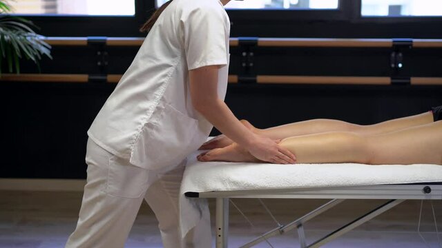Anonymous female physiotherapist massaging leg of crop woman