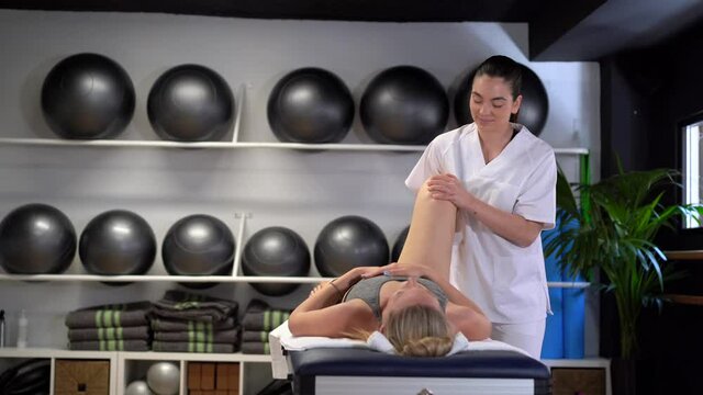 Delight female physiotherapist massaging leg of crop woman