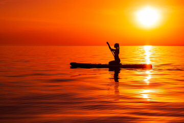 Girl on stand up paddle board at quiet sea with bright sunset or sunrise. Woman paddle on sup board in sea.
