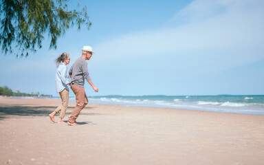 Fototapeta na wymiar Two retired Asian couples happily run hand in hand on the beach.