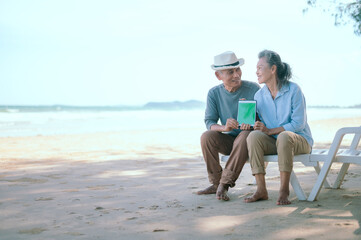 Elderly Asian couple holding laptops green sceen on the beach